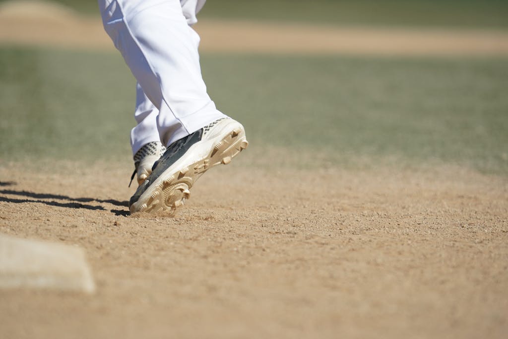 Athlete wearing white trousers in action on a baseball field, emphasizing movement.
